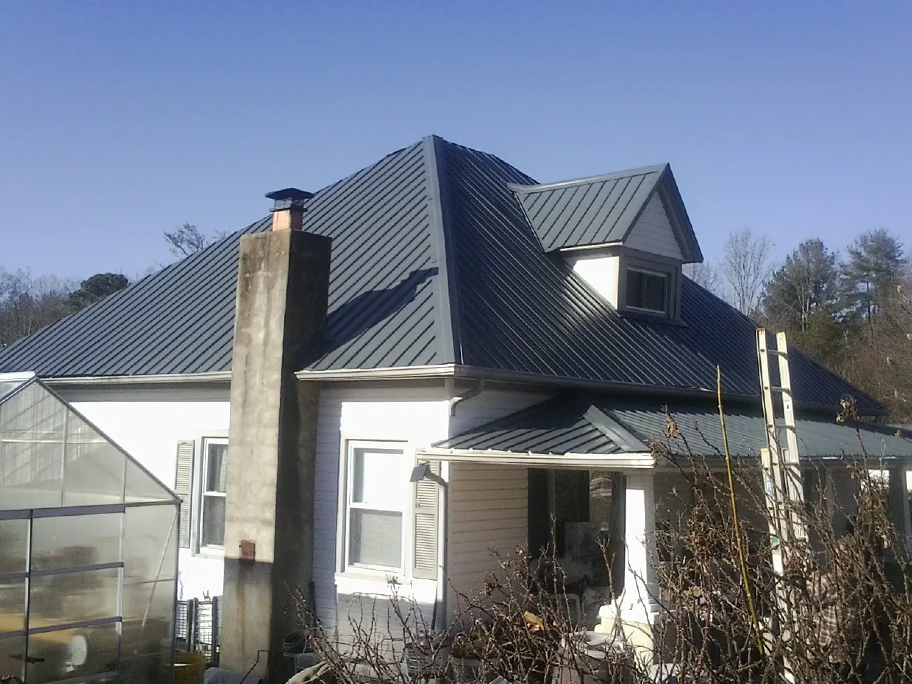 Dark blue standing seam metal roof on a white farmhouse with dormer — Slate & Tile Roof Repair by Roofing Brothers in Lewellen
