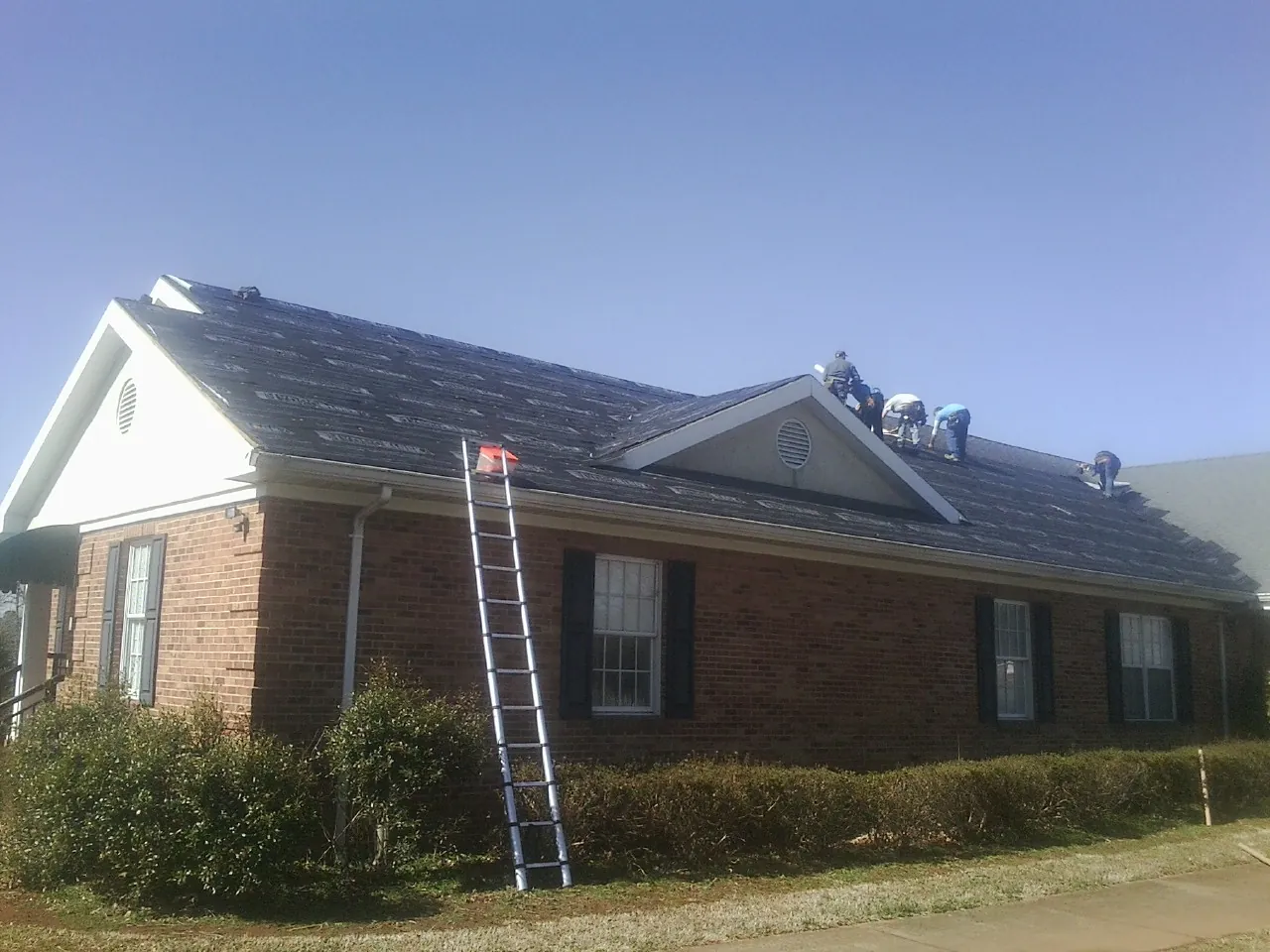 Crew tearing shingles off a brick ranch roof with a ladder set — Emergency Roof Repair work by our crew in Lewellen