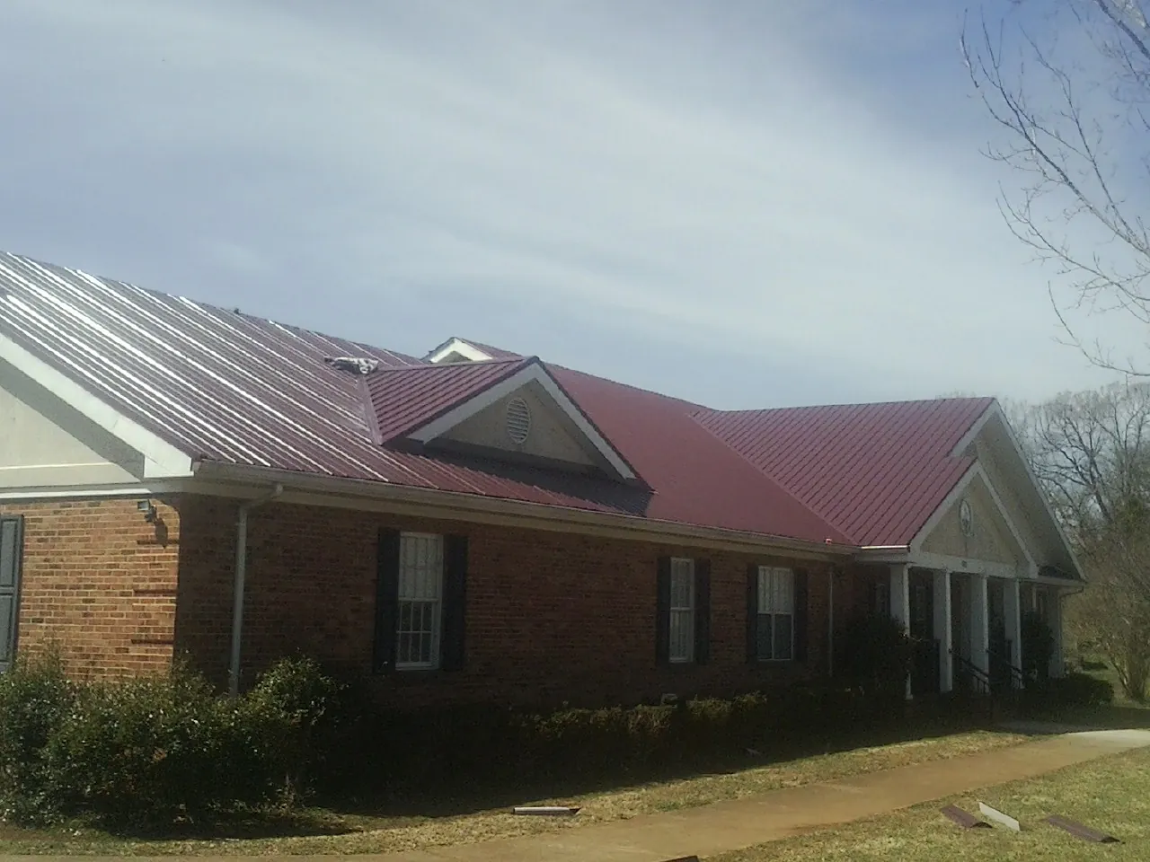 Red metal roof with gabled entries on a long brick building, from a Hail Damage Roof Repair job in Lewellen