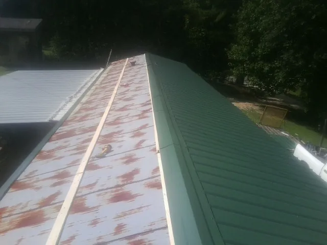Old rusted panels beside newly installed green metal roofing — Wind Damage Roof Repair by Roofing Brothers in Lewellen