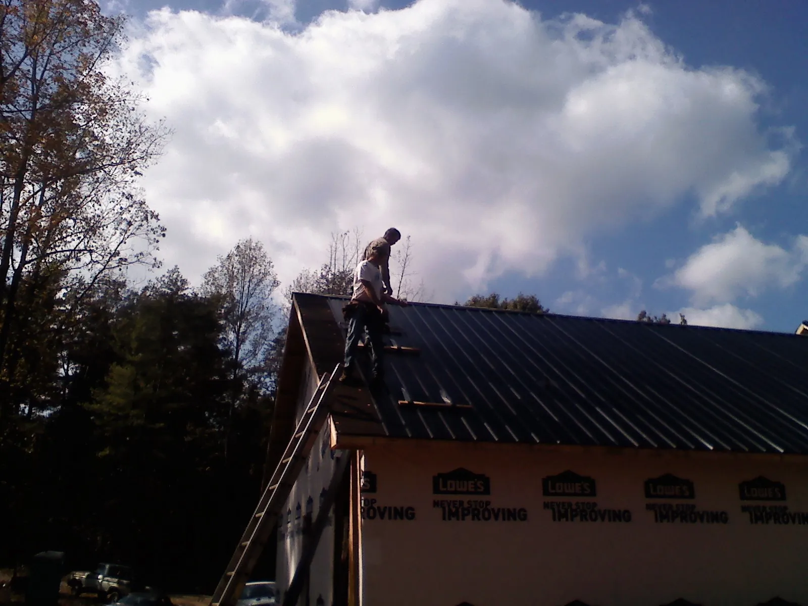 Roofer fastening dark metal panels high against a cloudy sky, from a Roof Inspection job in Lewellen