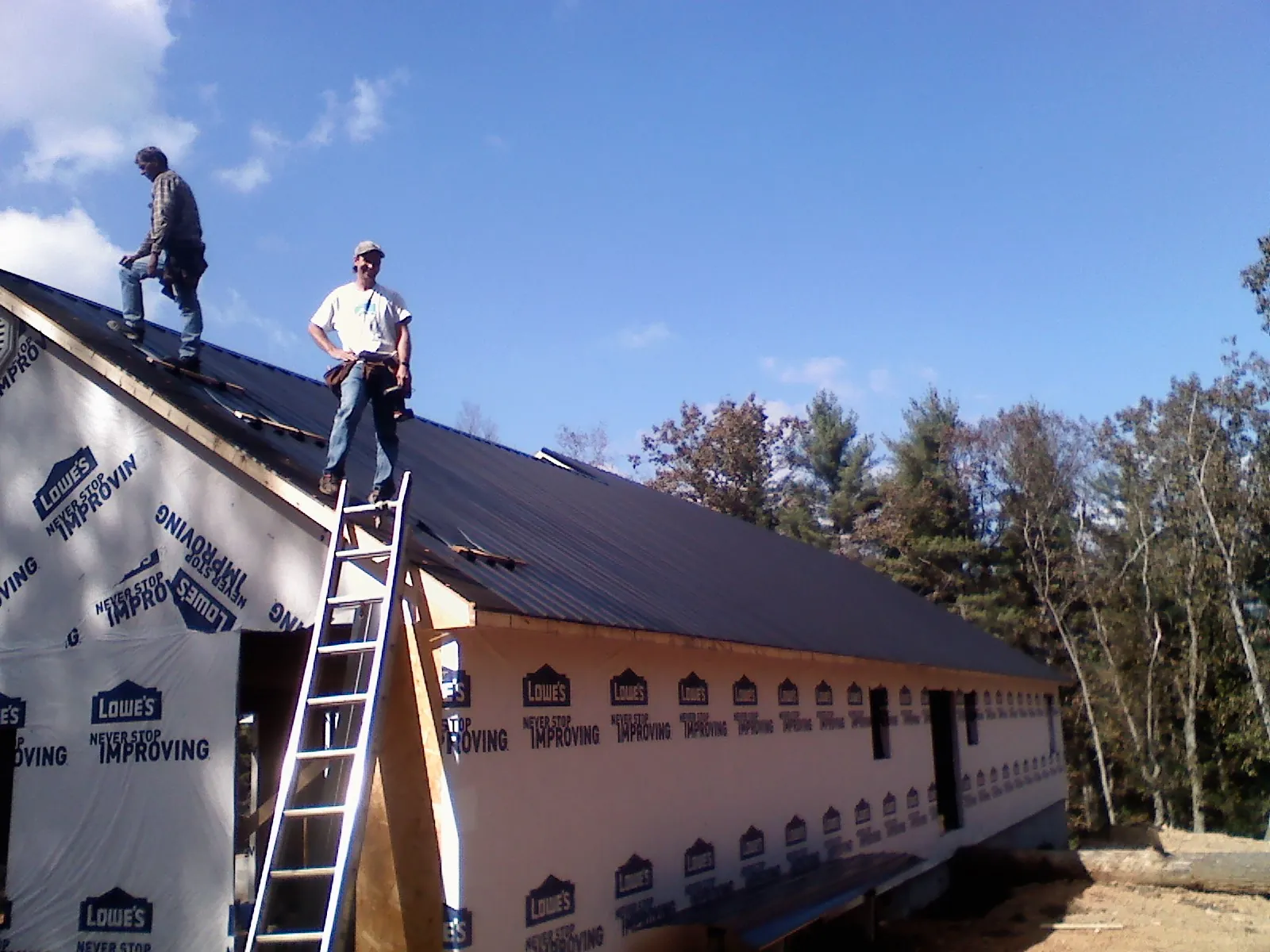Two roofers standing on a long dark metal roof over a wrapped building in Lewellen