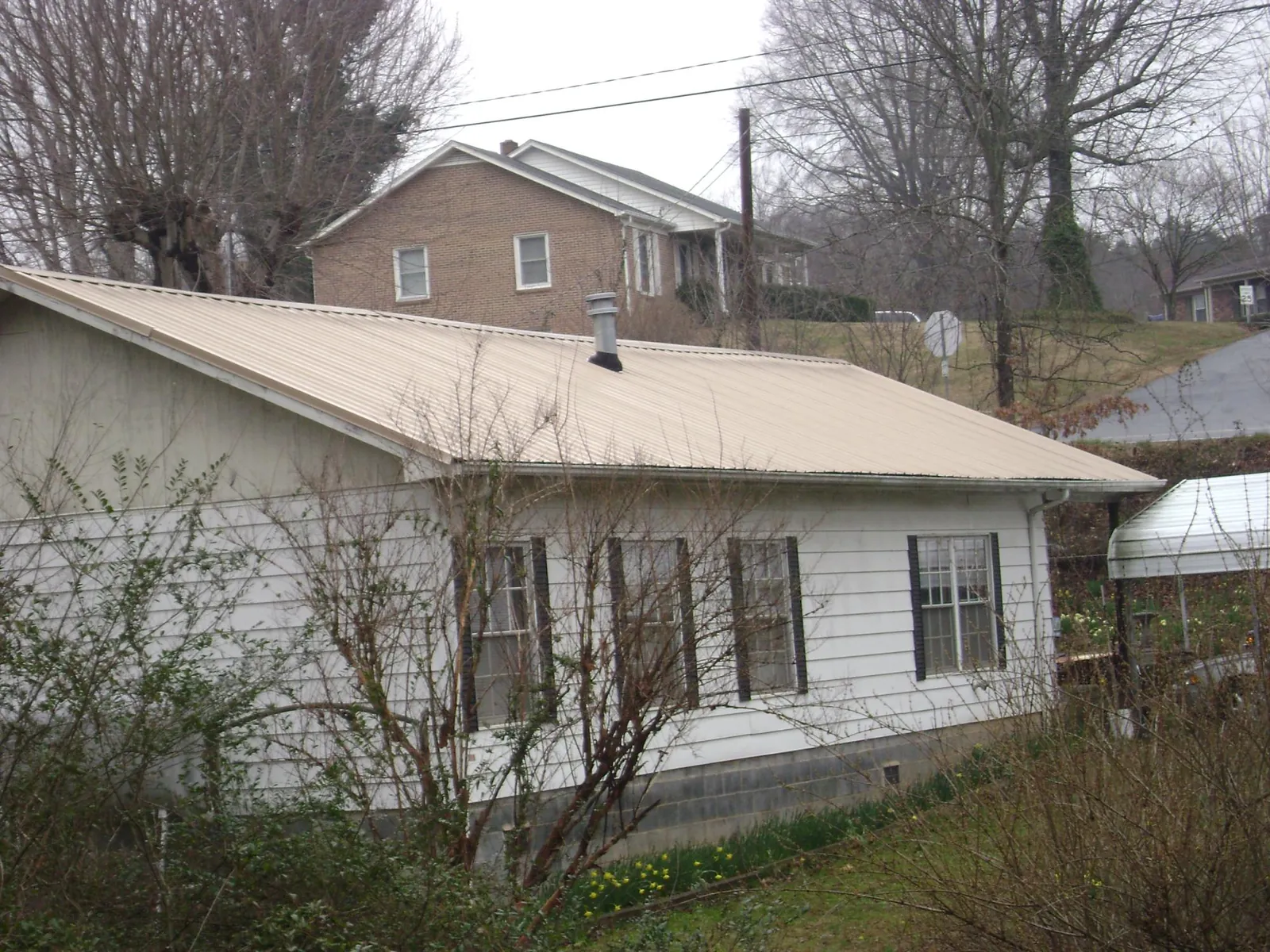 Tan metal roof on a white sided house set into a hillside — Commercial Roofing by Roofing Brothers in Lewellen
