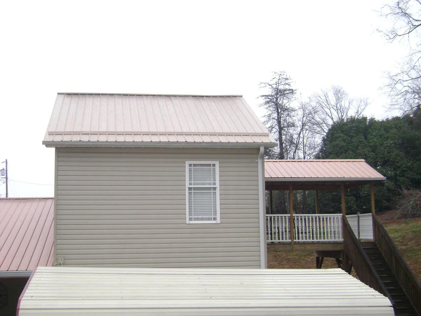 Tan metal roofs on a two story addition and attached porch, from a Roof Replacement job in Lewellen